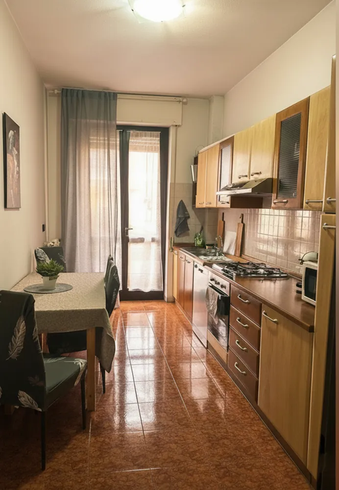 La cucina abitabile con i mobili in legno, il piano cottura e il tavolo accanto alla porta finestra